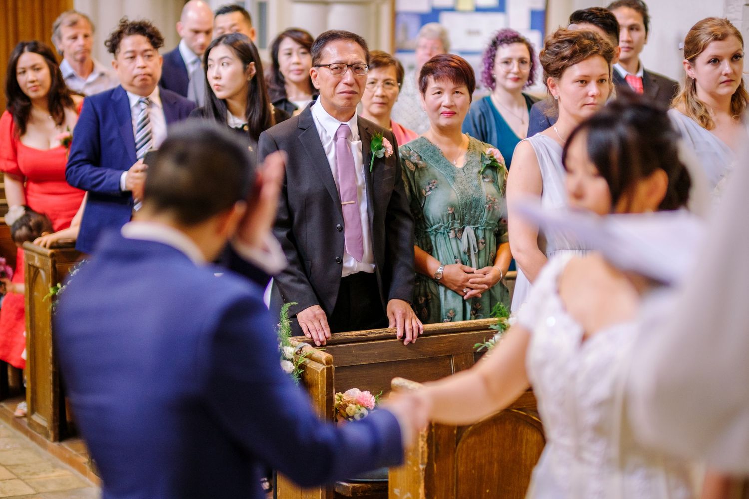 Wedding guests react with joy and emotion during a ceremony in a church setting.