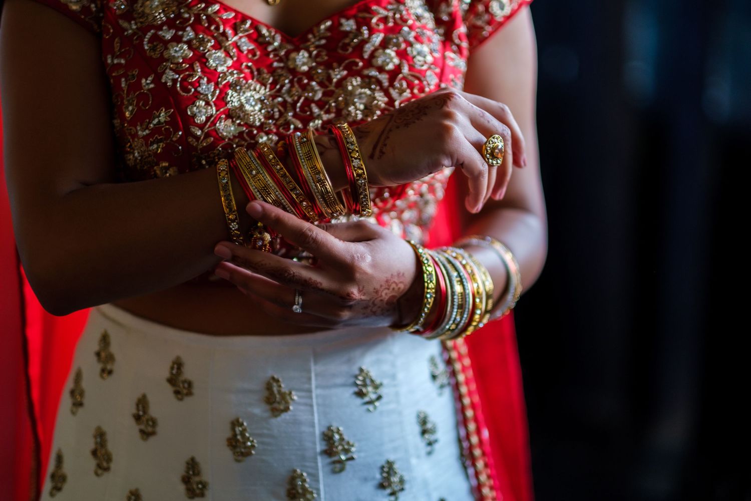 Close up of bridal hands adorned with bangles and jewelry wearing traditional Indian wedding attire.