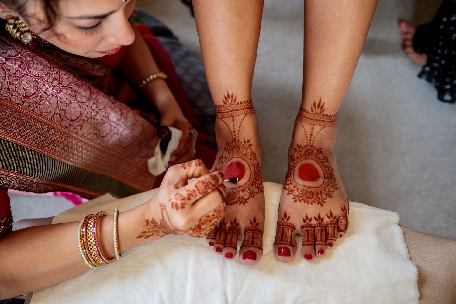 Intricate henna designs being applied to hands and feet during traditional wedding preparations.