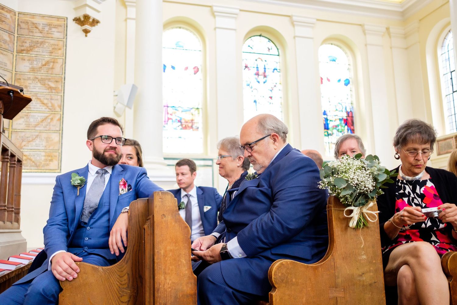 Guests seated in rows at an elegant wedding ceremony with stone walls and stained glass windows in the background.