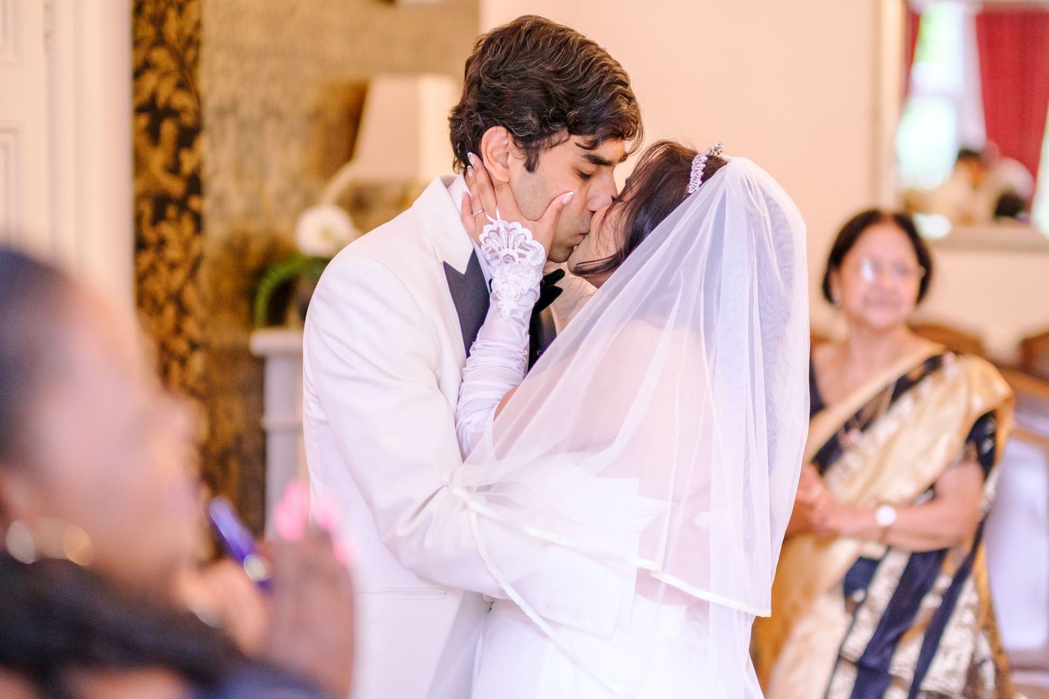 A romantic first kiss between newlyweds at their wedding ceremony while guests look on.