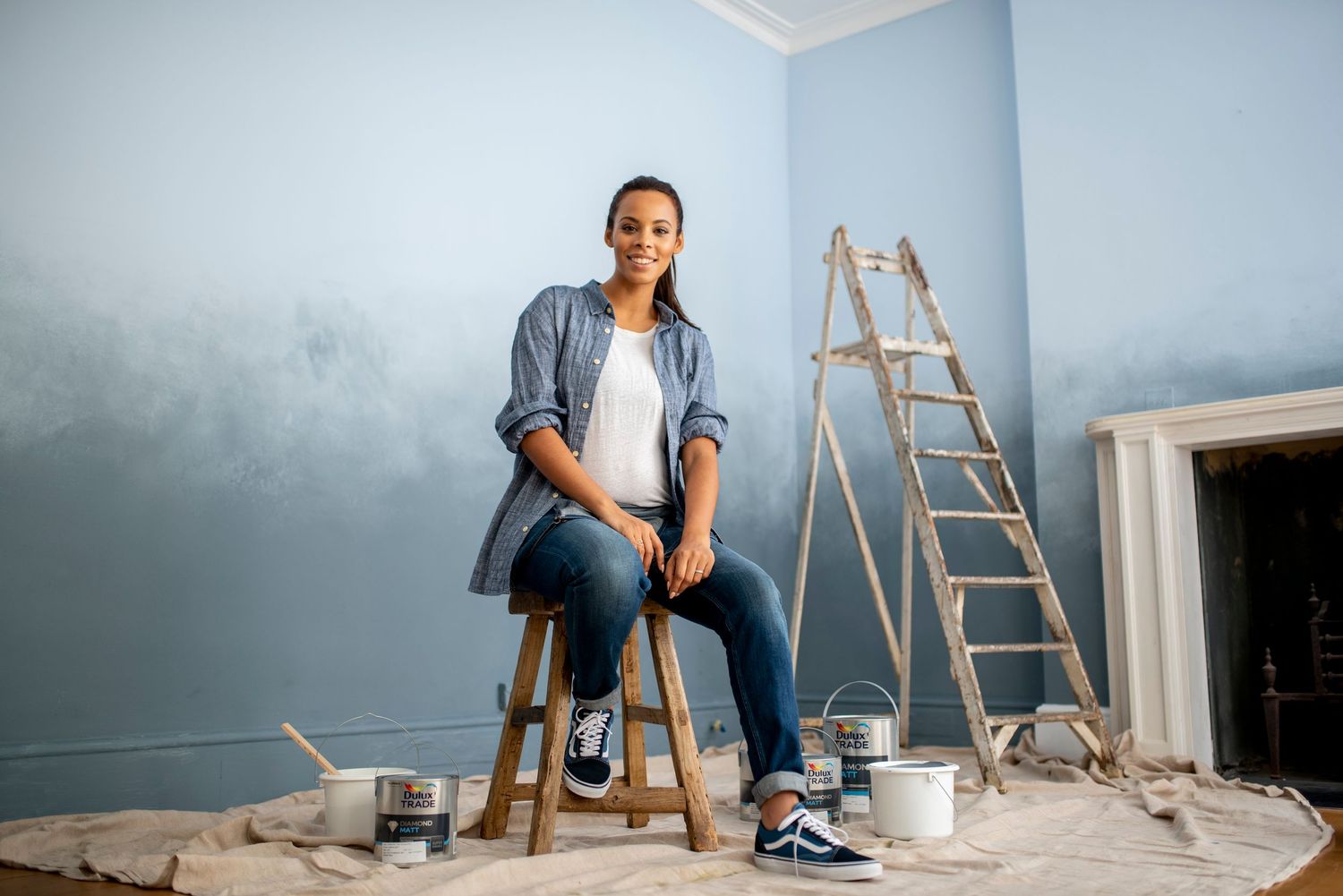 Room undergoing renovation with blue walls, paint supplies, and a ladder visible.