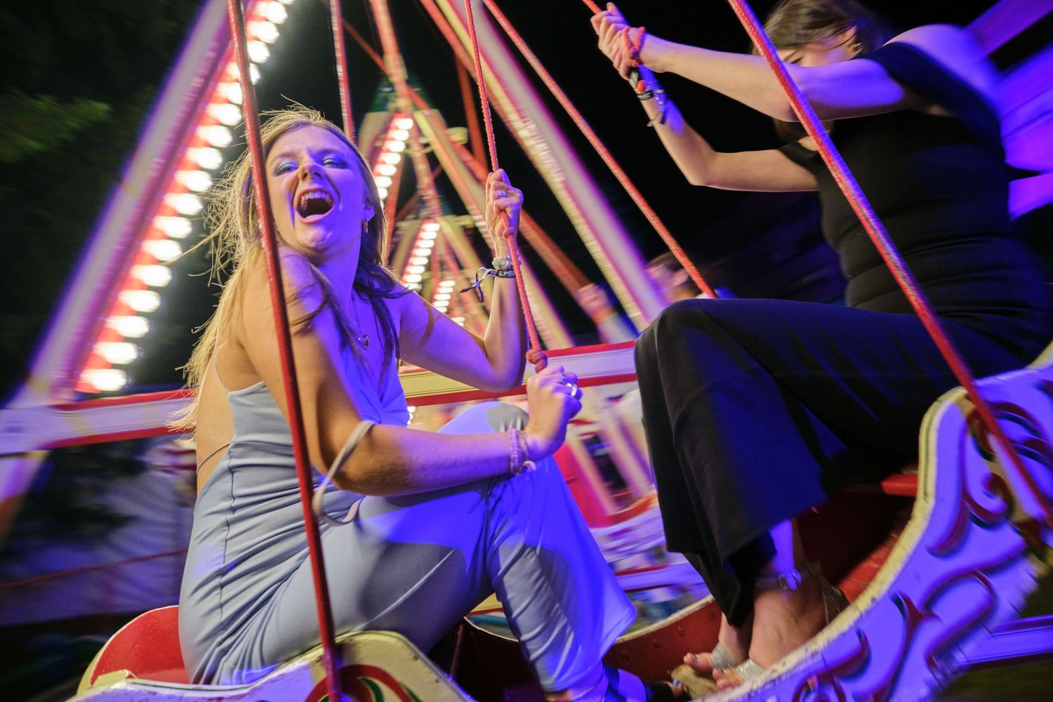 People enjoying a colorfully lit carnival ride at night with joyful expressions.