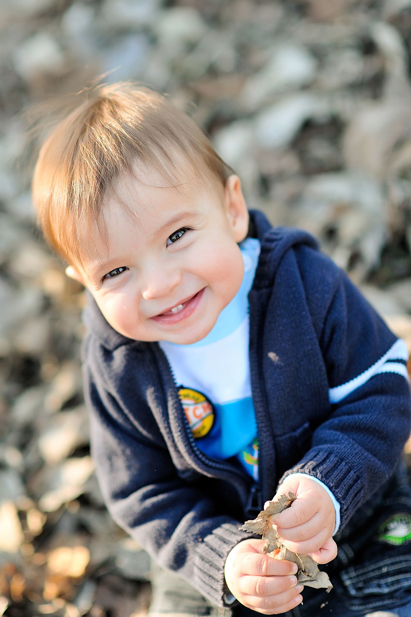 Child in navy blue jacket sitting outdoors enjoying a snack in natural lighting.