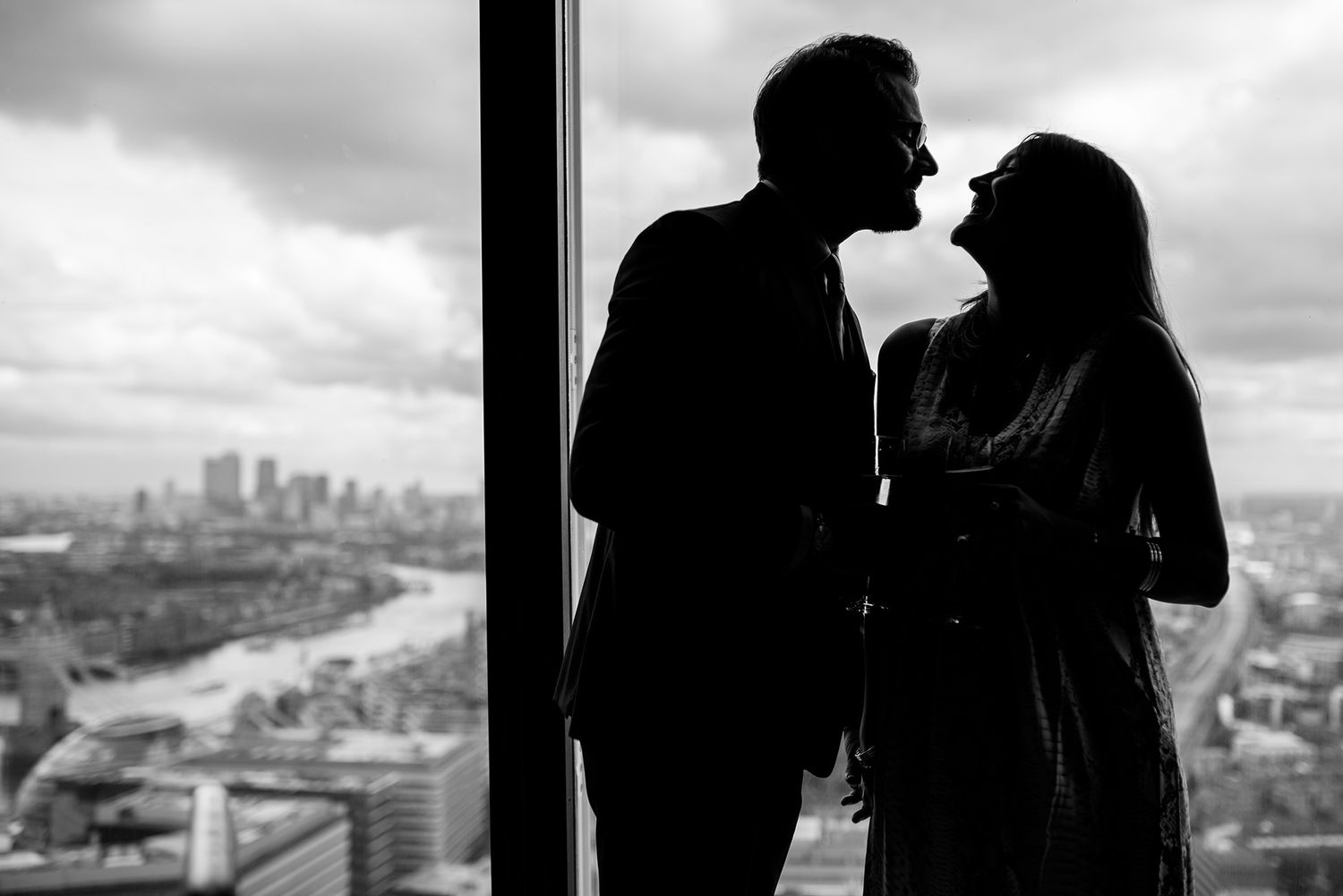 Silhouettes of a couple stand against a cityscape view through large windows.