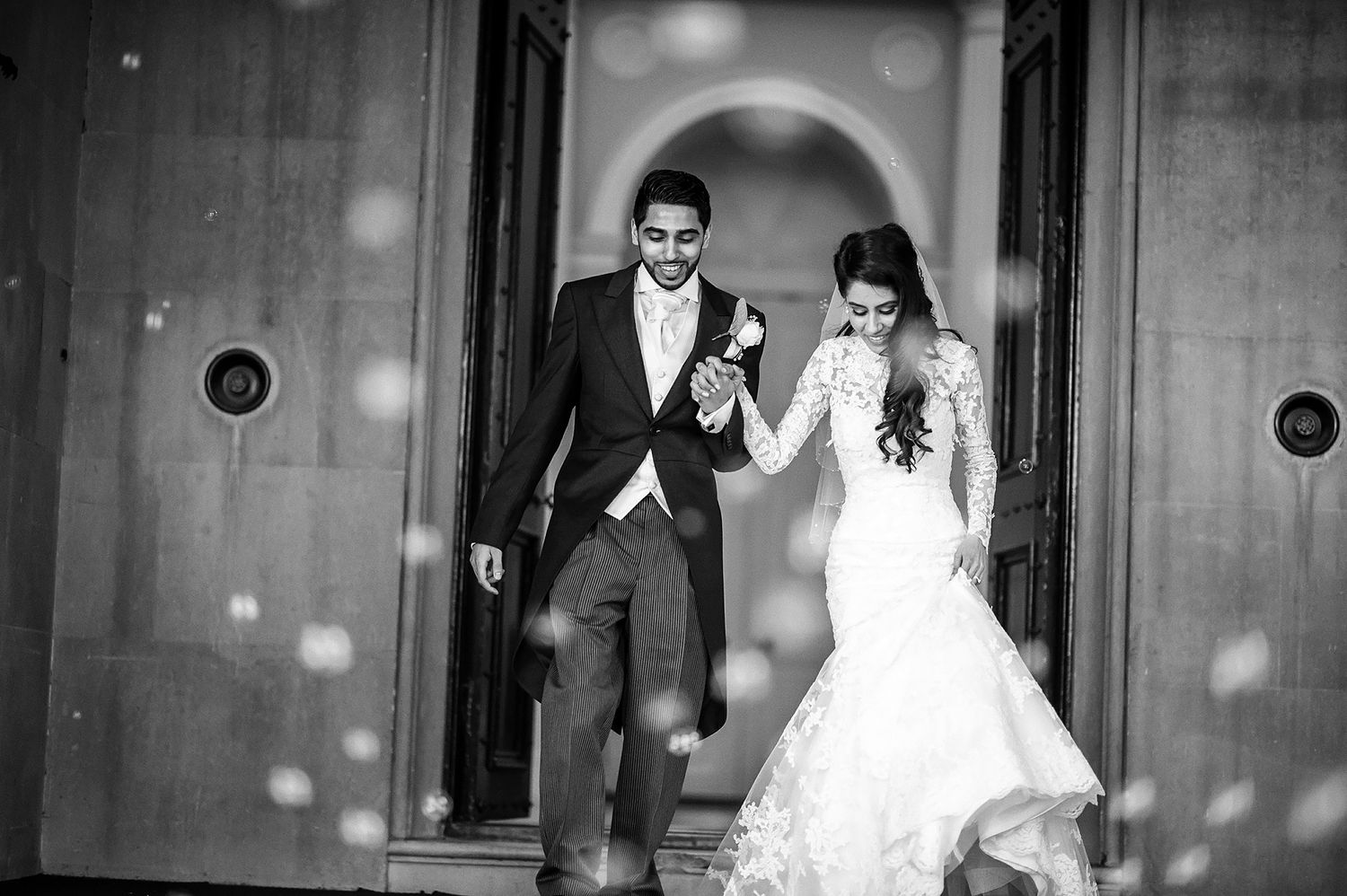 Black and white image of couple joyfully exiting venue through arched doorway.