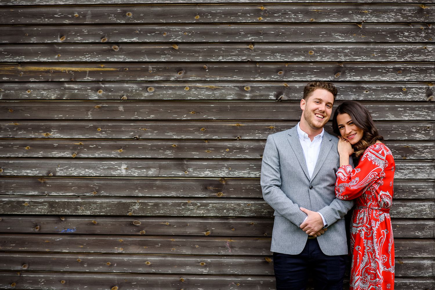 A couple poses together against a rustic wooden wall background.