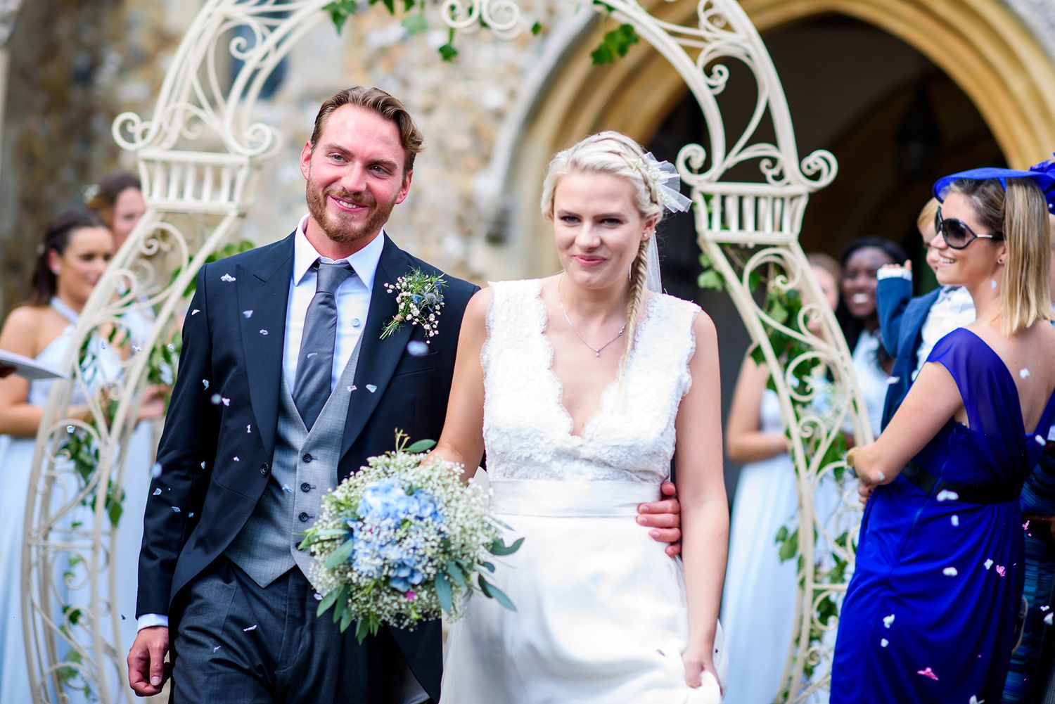 Outdoor wedding ceremony under an ornate white arch decorated with blue and white flowers.