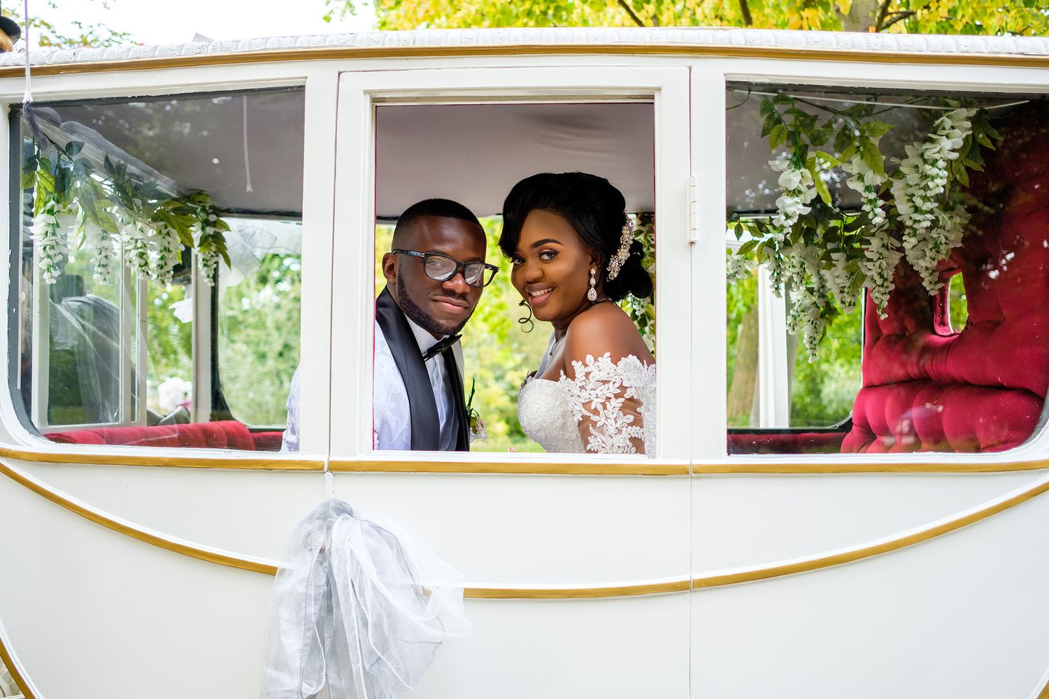 Wedding party riding in a decorated white carriage through a scenic outdoor setting.