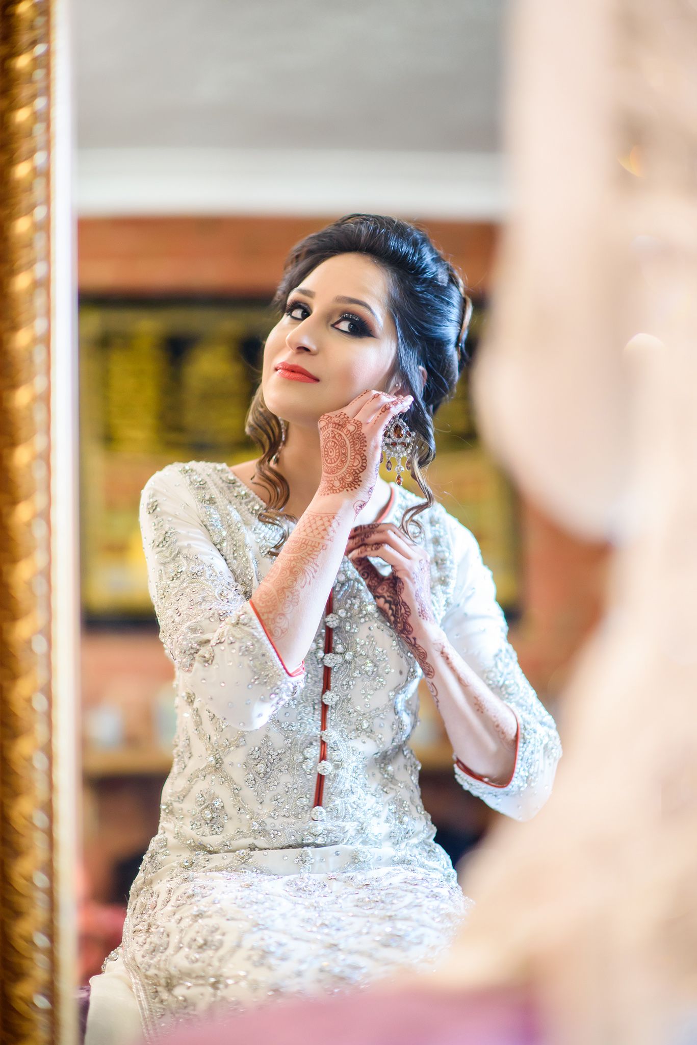 Person in white lace dress with elegant makeup detail against gold-framed background.
