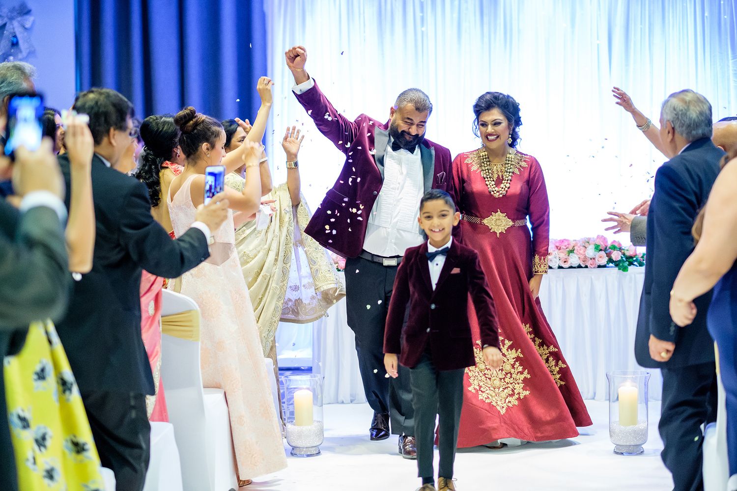 Wedding celebration with guests cheering during a grand entrance in a decorated reception hall.