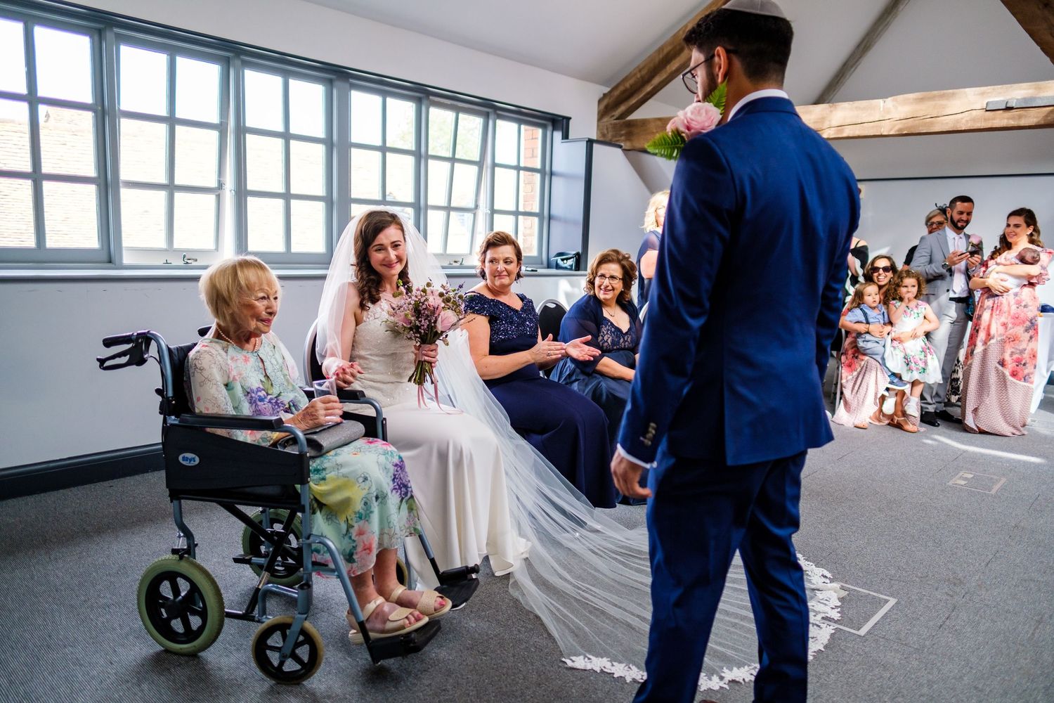 Wedding ceremony guests gathered in a bright modern room with large windows.