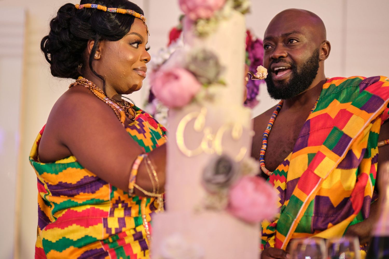 People in colorful traditional African kente cloth attire dancing and celebrating at a festive gathering.