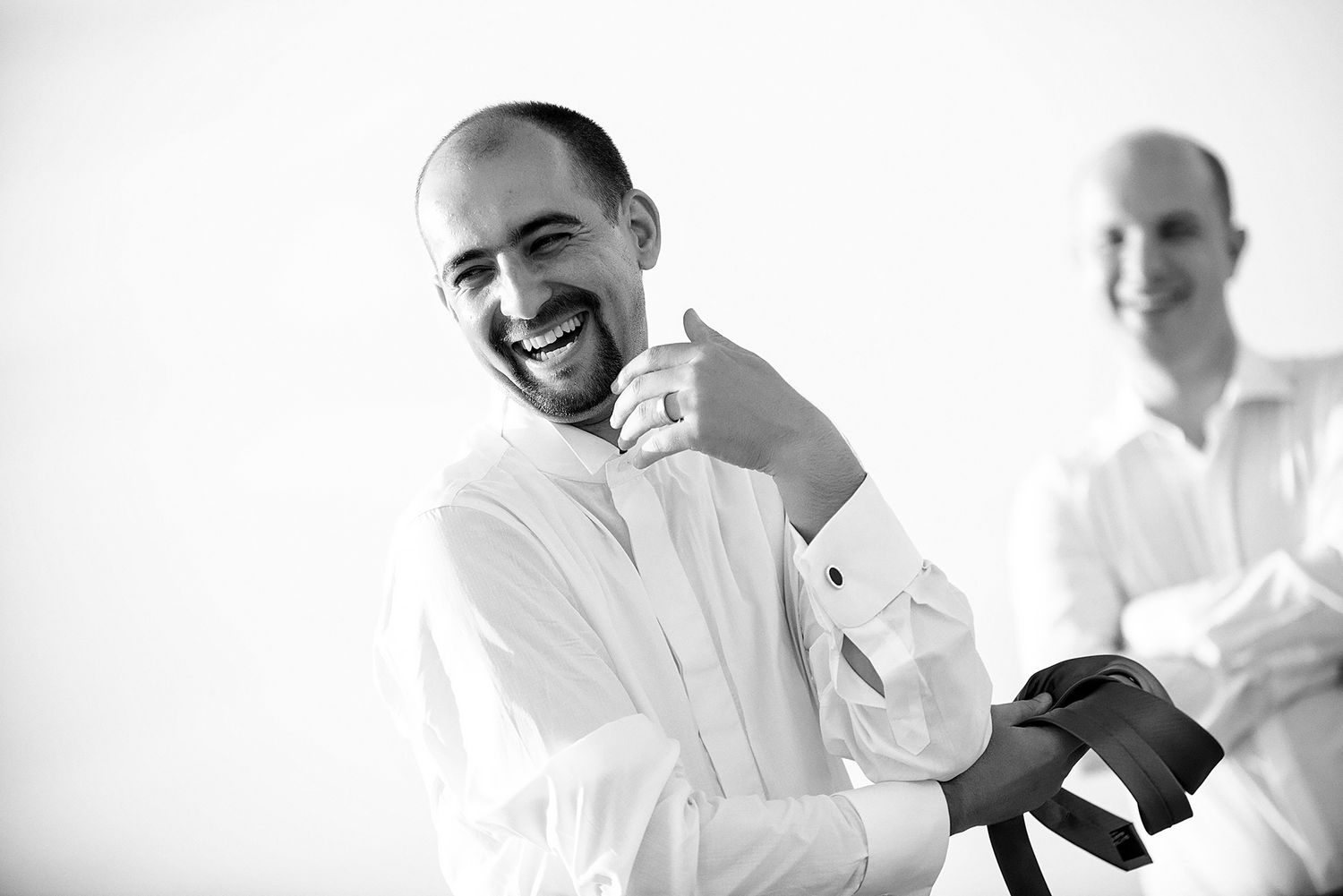 Two people in white dress shirts getting ready for a formal event with joyful expressions.