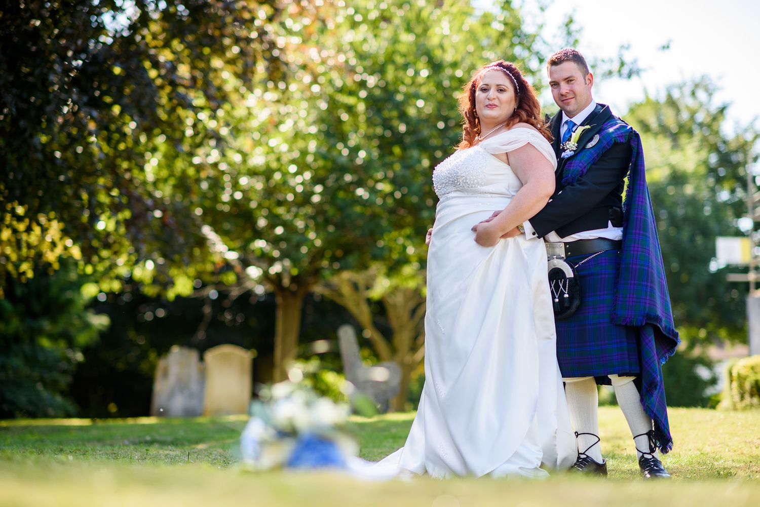 Wedding couple posing together in a sunlit garden setting.