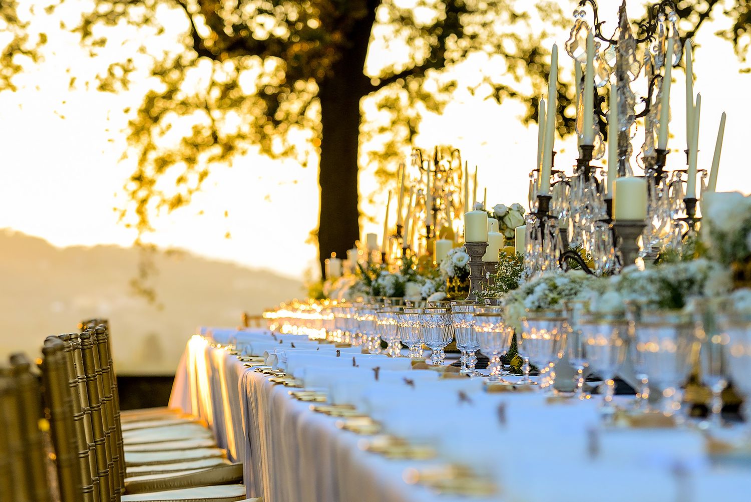Elegant outdoor wedding reception table settings with crystal candelabras at golden hour.