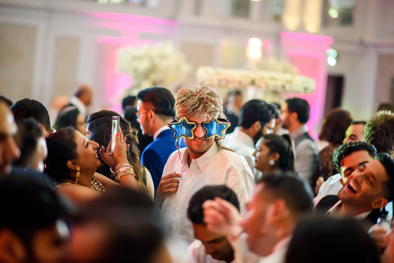 Energetic wedding reception with guests dancing under pink and purple lighting.