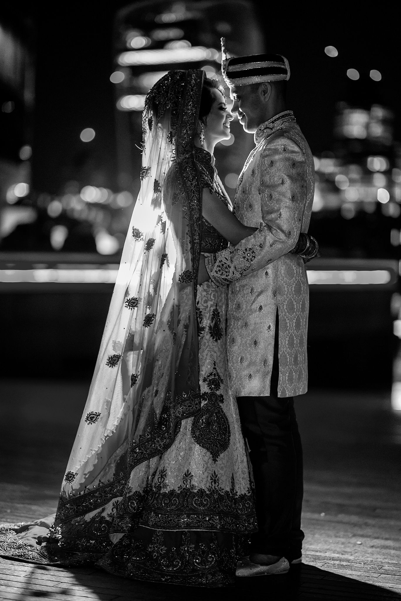 Black and white portrait of a couple in traditional wedding attire against a city nightscape.