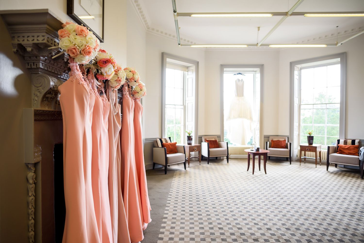 Peach colored bridesmaid dresses hang in a spacious venue room with patterned carpet.