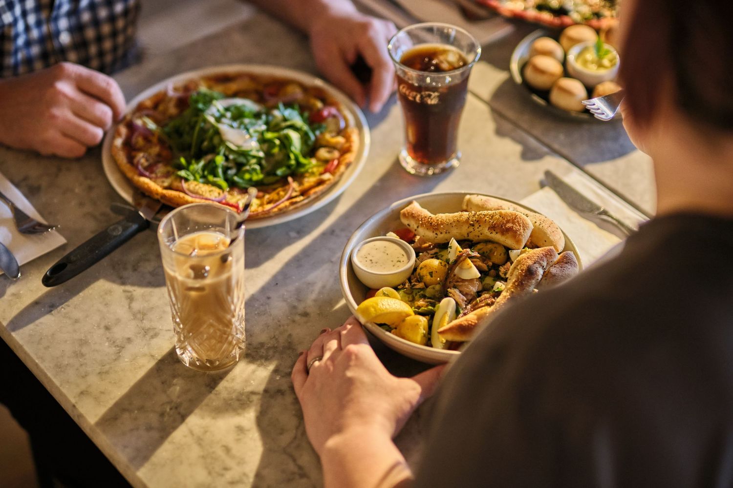 Friends enjoying pizza and drinks together at a restaurant table with various dishes and beverages.