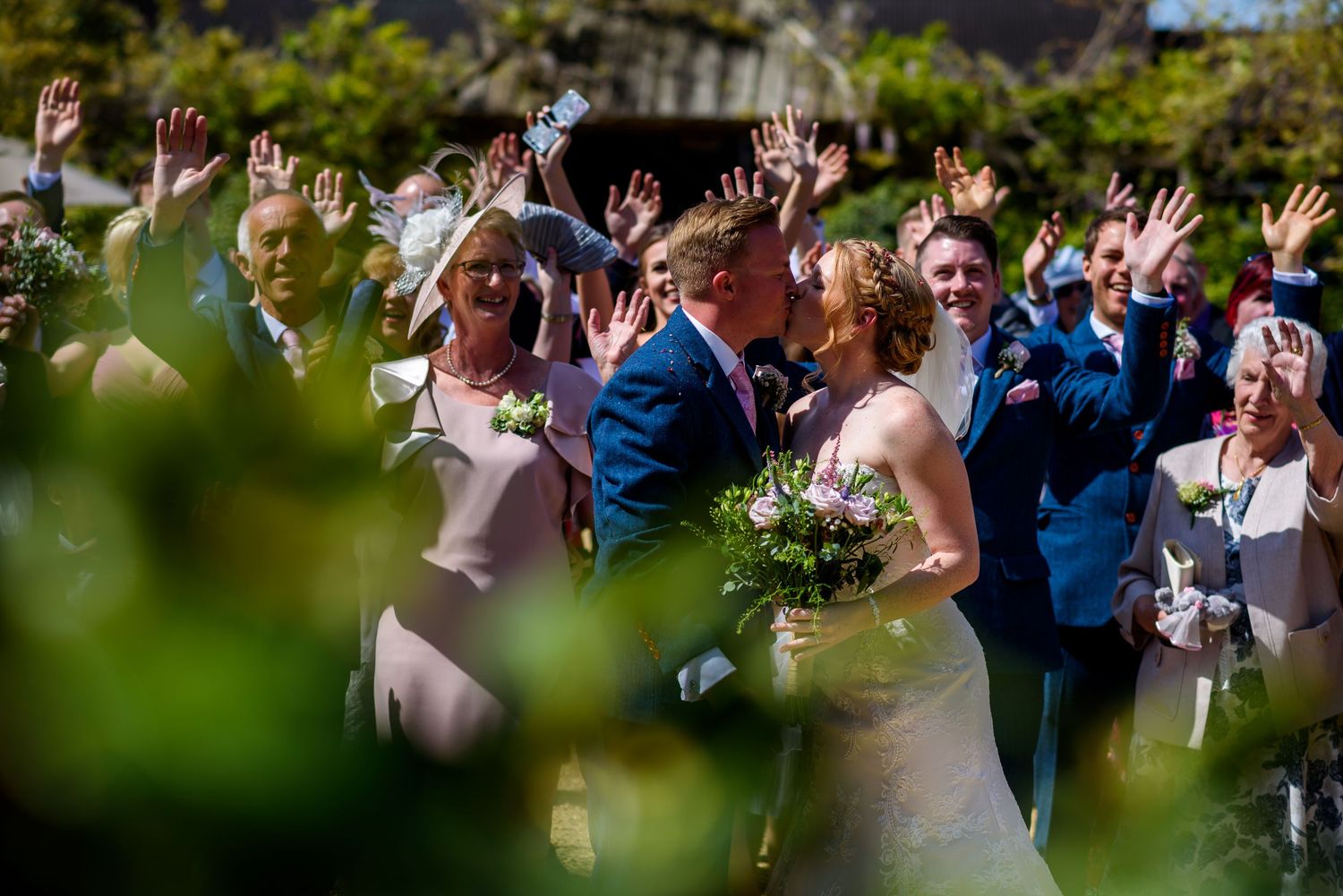 Joyful wedding party and guests throwing confetti in garden setting.