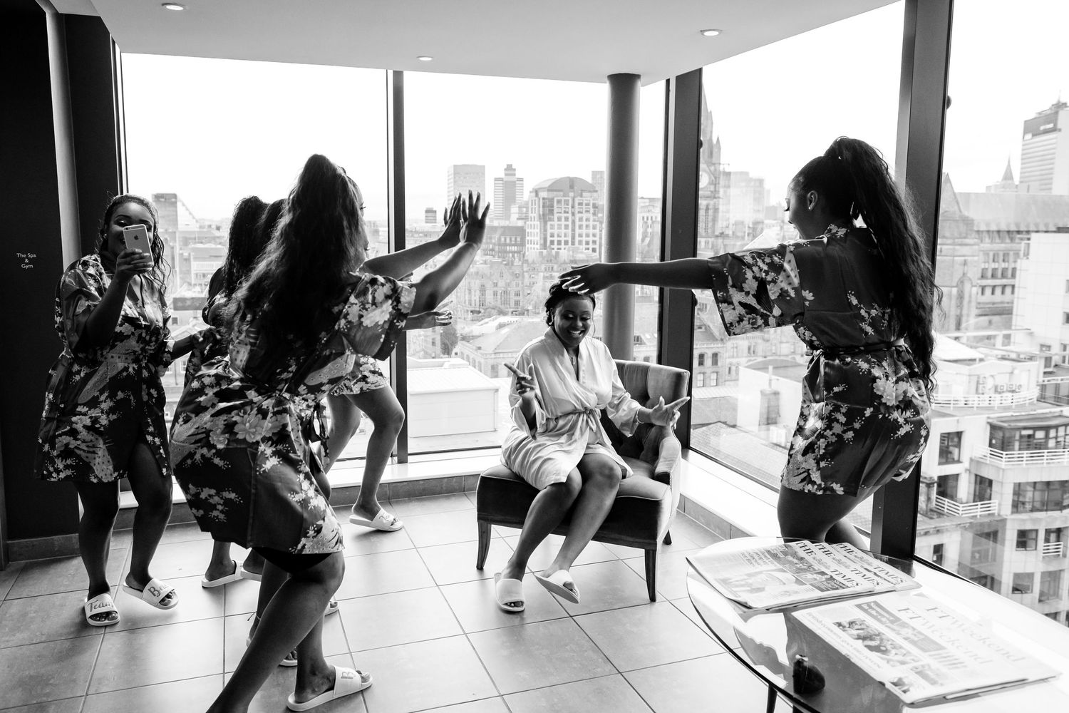 Wedding guests dancing and socializing in a modern venue with large windows overlooking a city skyline.
