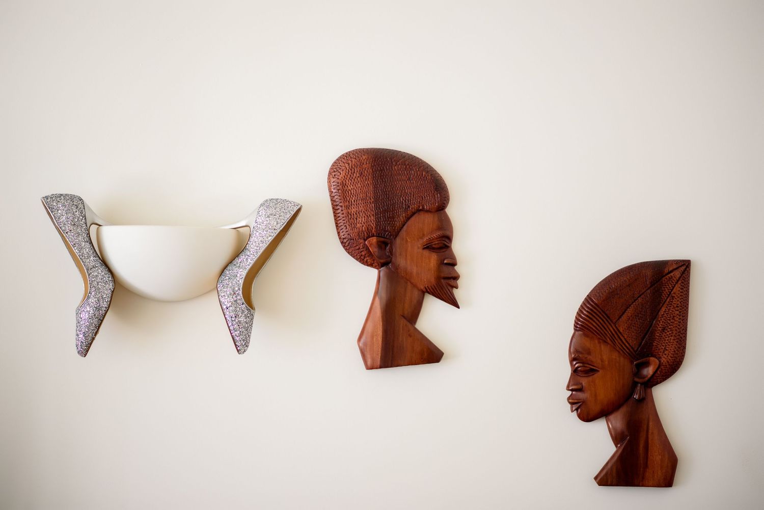 Decorative wall art featuring carved wooden African profile sculptures and a white abstract wall sconce.