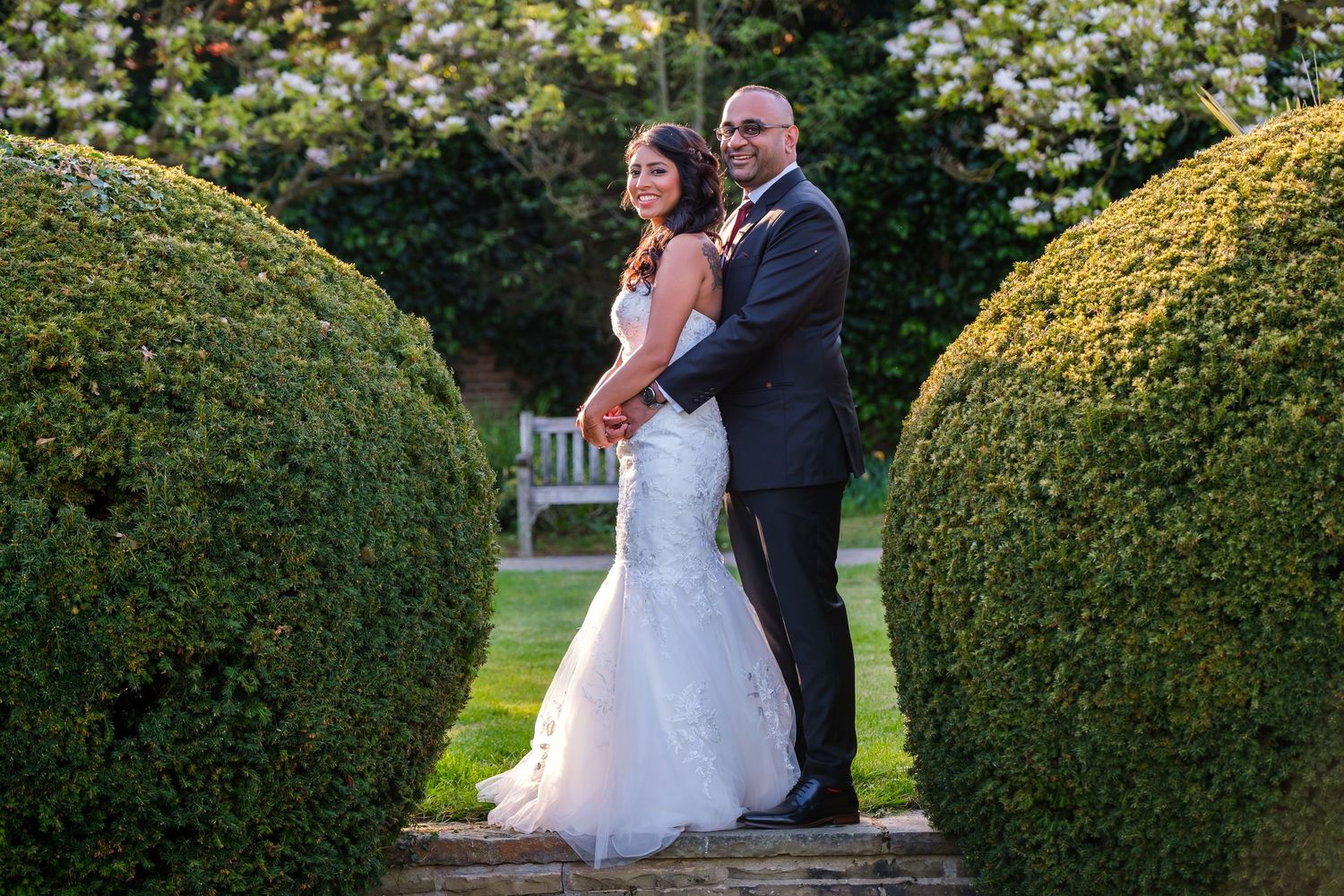 Romantic wedding couple portraits taken in a manicured garden with sculpted hedges and natural greenery.