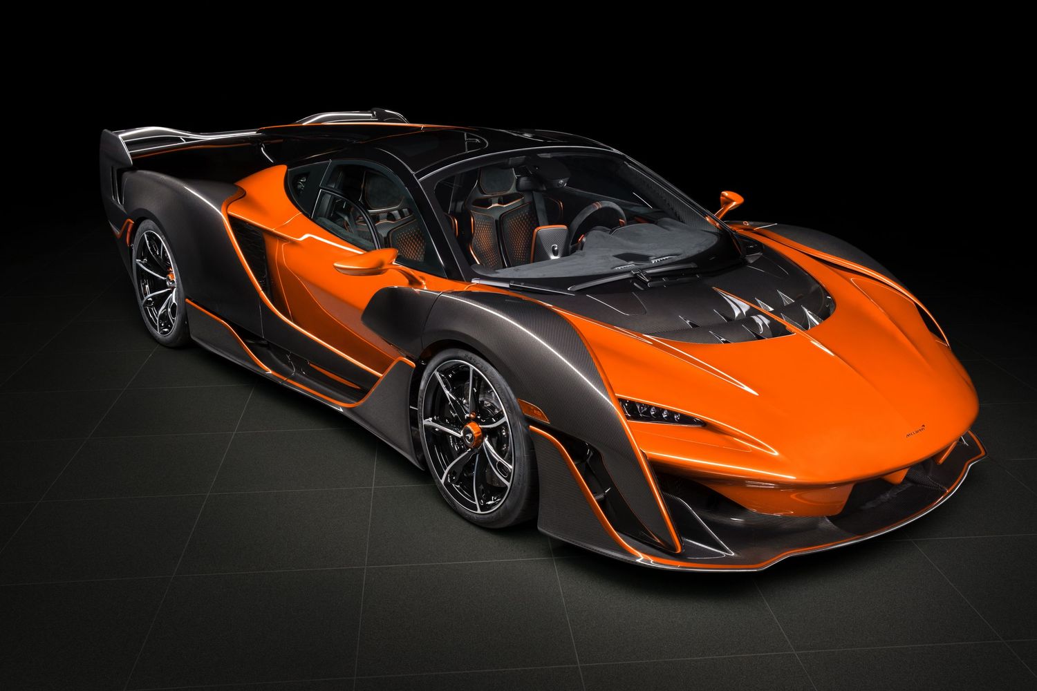 Side profile of a sleek orange McLaren supercar showcasing its aerodynamic curves and black accents.