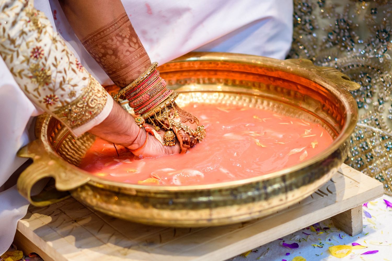 Close-up of henna-decorated hands performing a traditional ritual with a copper plate.