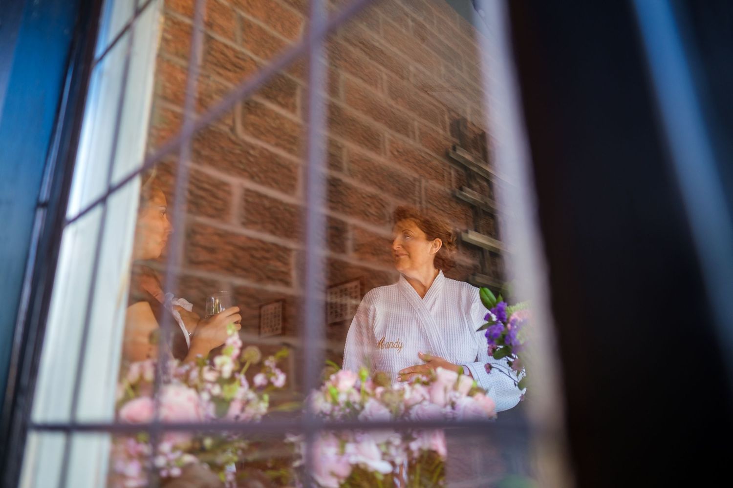 A couple shares a romantic dance in a rustic brick-walled venue with soft purple lighting and floral decorations.