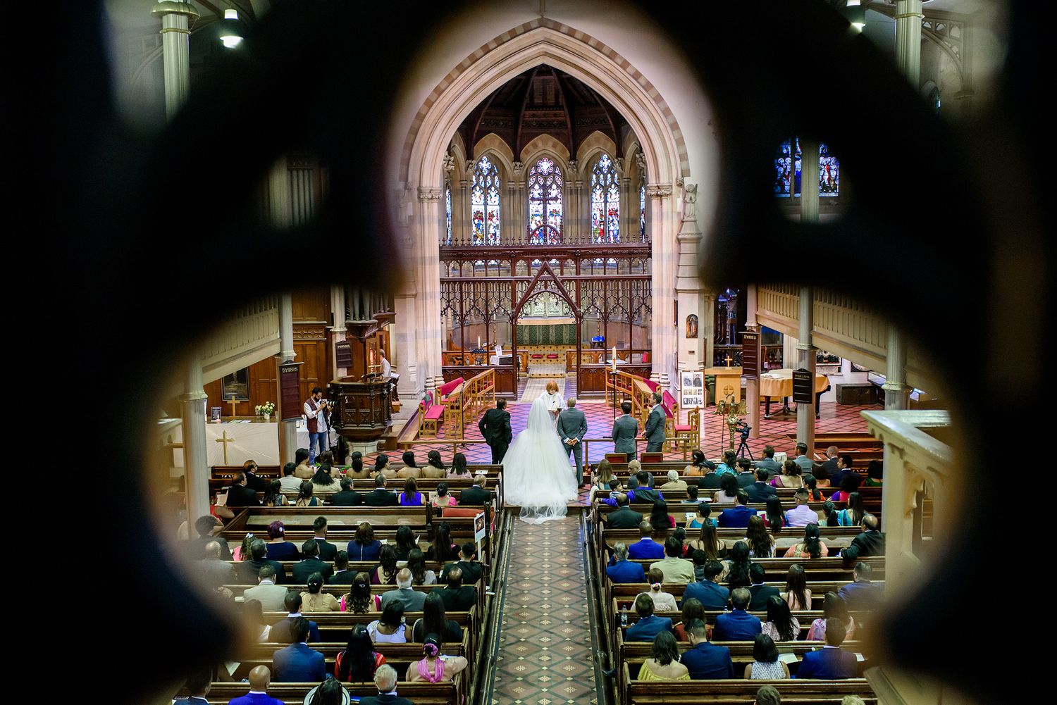 Wide angle view of a grand church wedding ceremony with guests seated in wooden pews.
