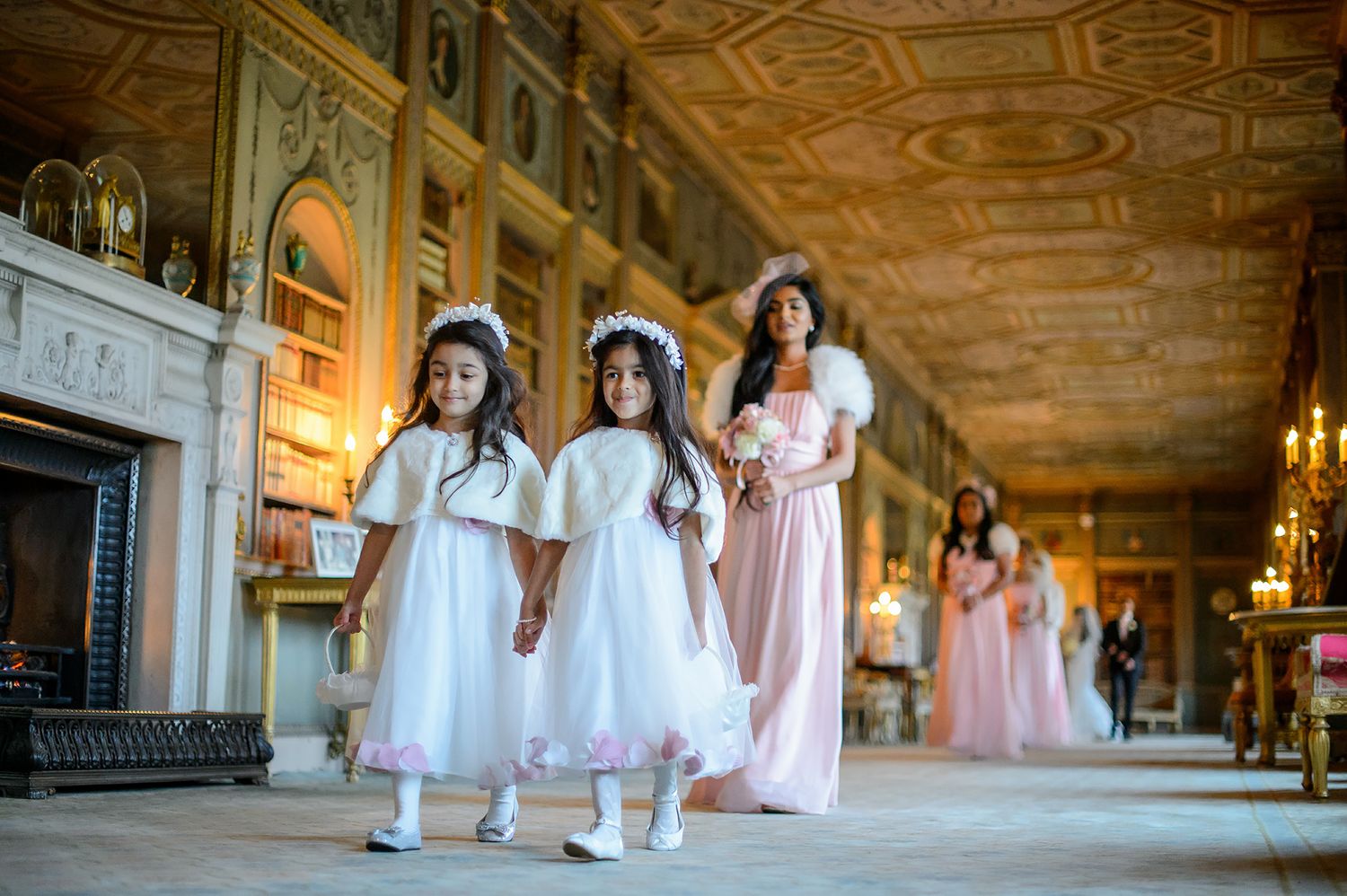 Bridesmaids in blush pink dresses gathered in an elegant hallway with ornate ceiling details.