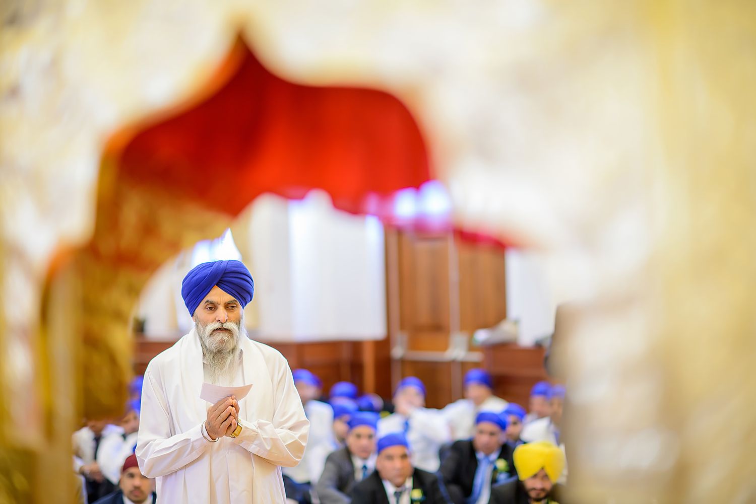 Sikh wedding ceremony taking place in golden-lit indoor venue.