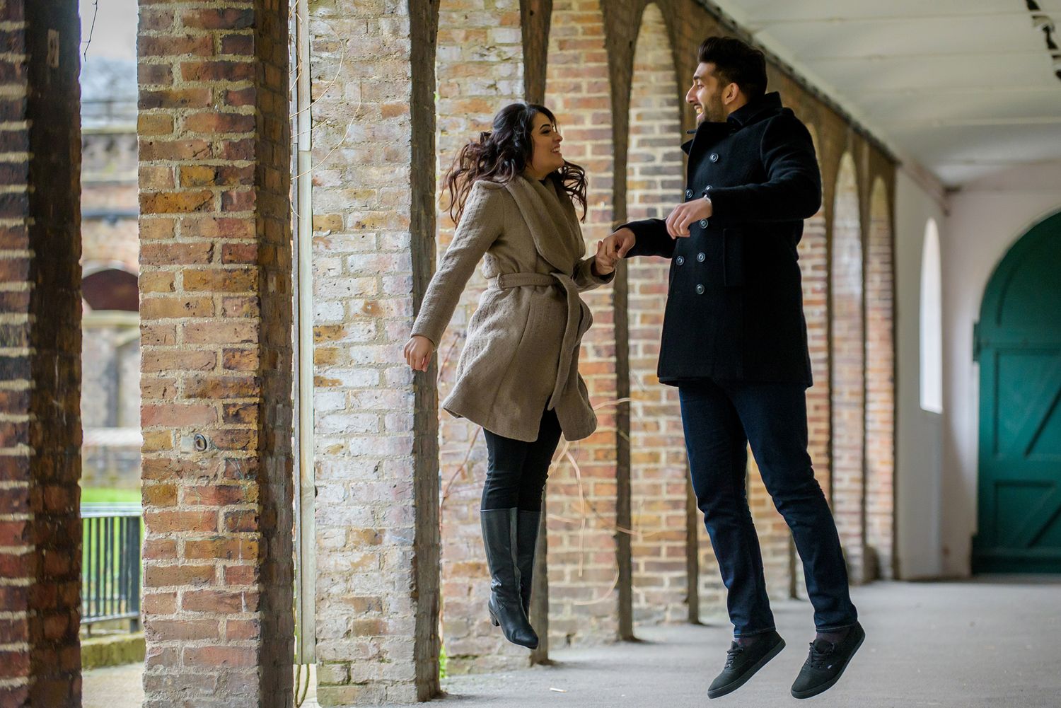 People interacting playfully in an outdoor brick colonnade walkway.