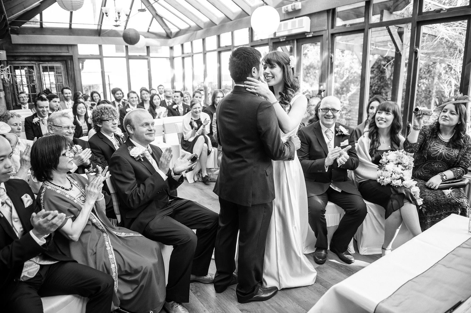 Wide angle view of wedding reception in a sunlit conservatory filled with guests.