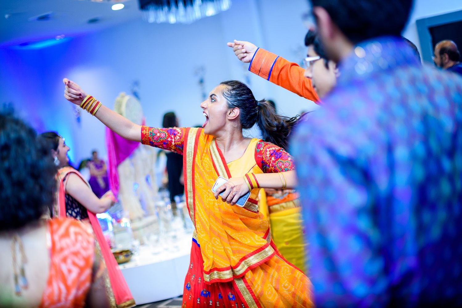 Artistic blue-tinted photo capturing dancers in bright orange traditional outfits during a performance.