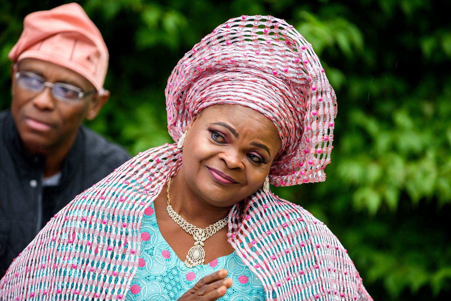 Wedding guests wearing traditional African head wraps and formal attire smile together outdoors.