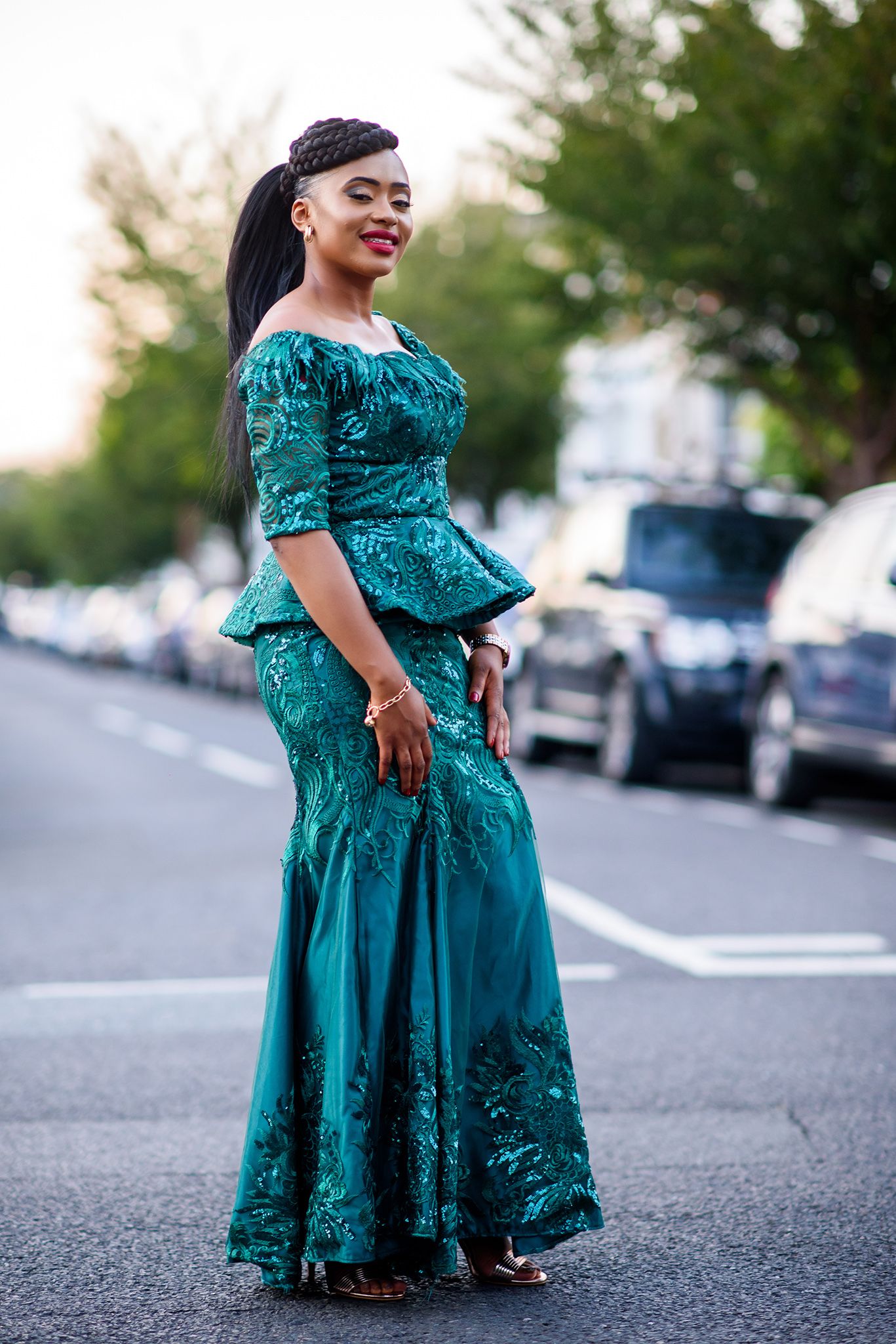 A person in a sparkling teal formal dress poses elegantly on a street at dusk.
