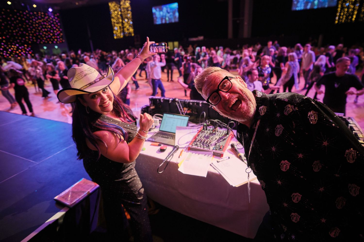 DJs performing at an energetic nightclub event with a large crowd dancing under purple lighting on the dance floor.