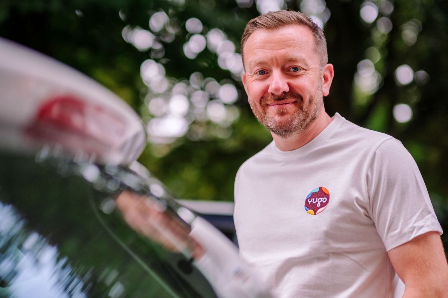 A white t-shirt with small logo seen outdoors with bokeh background lighting.
