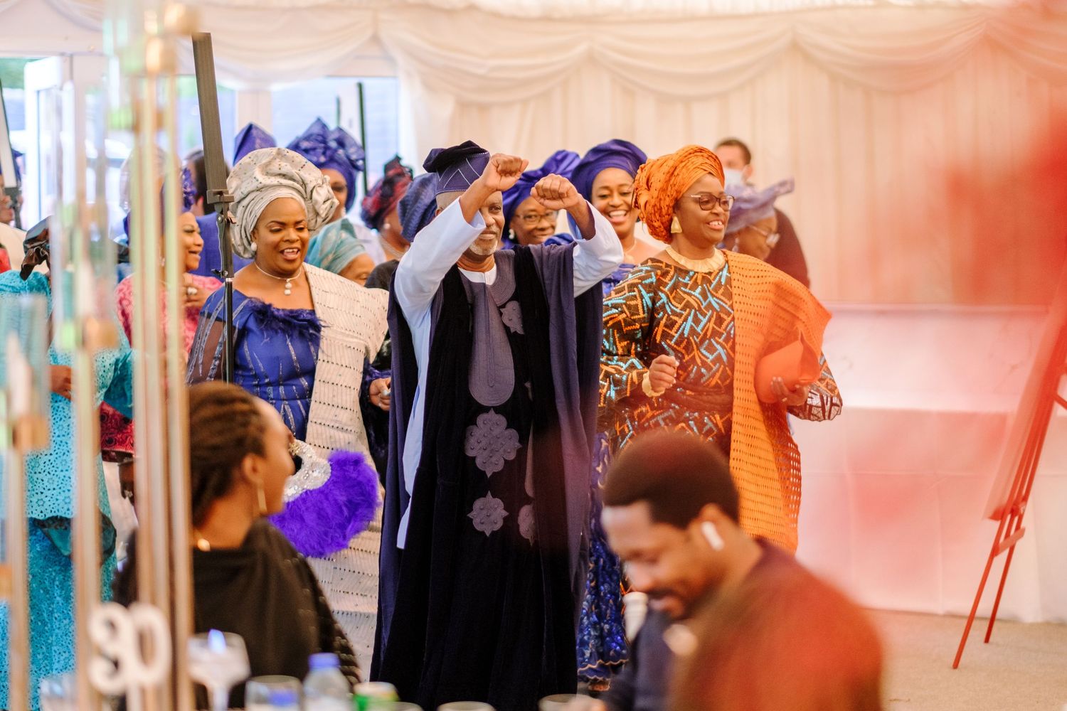 Wedding reception guests mingle and socialize in an elegantly decorated venue with pink lighting.