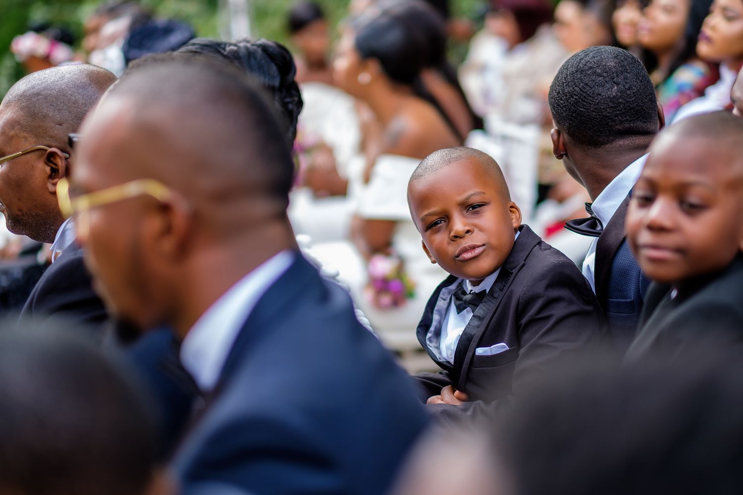 Wedding guests in formal attire gathered for an outdoor ceremony.