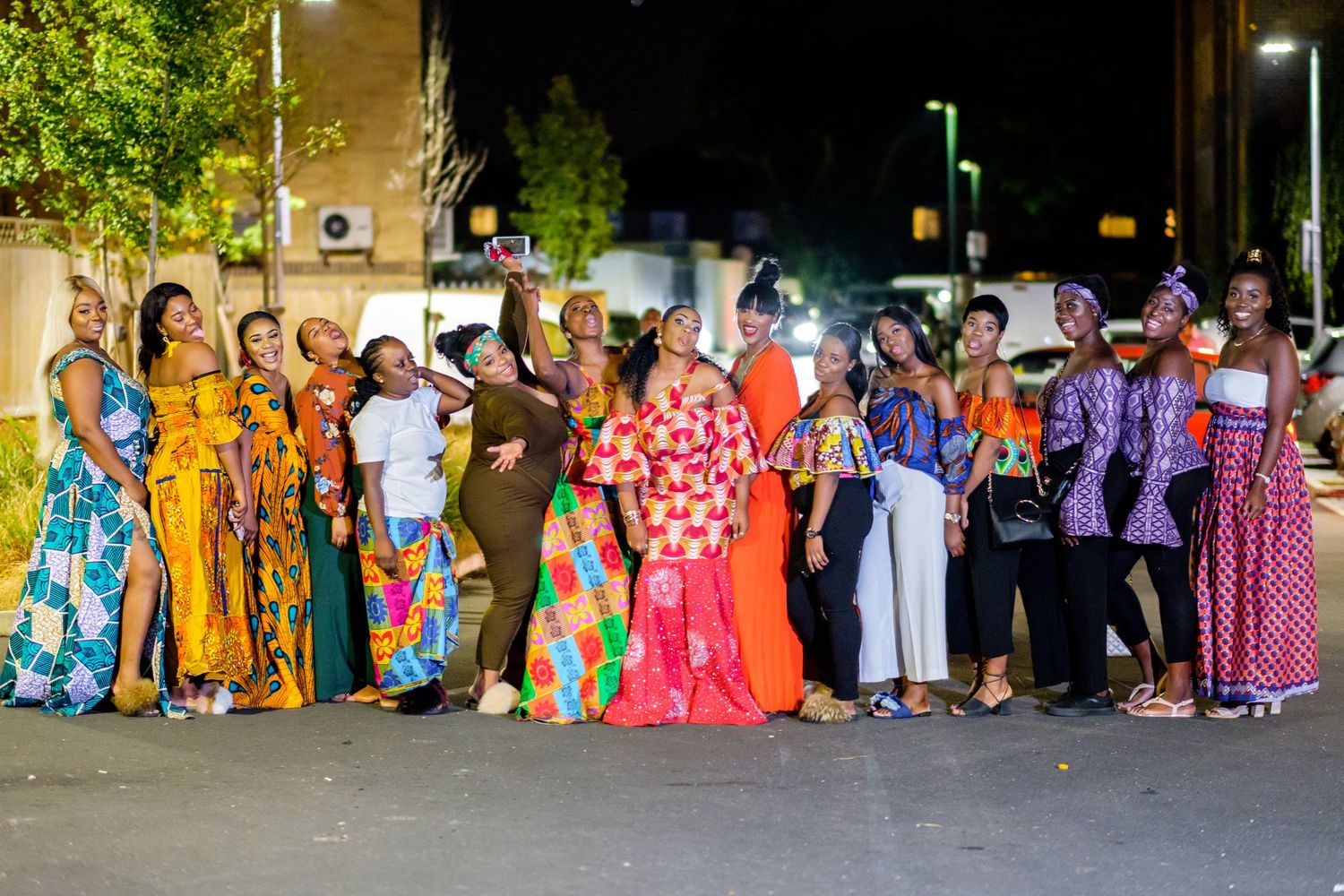 Large group photo of colorfully dressed wedding guests gathered outside at night.
