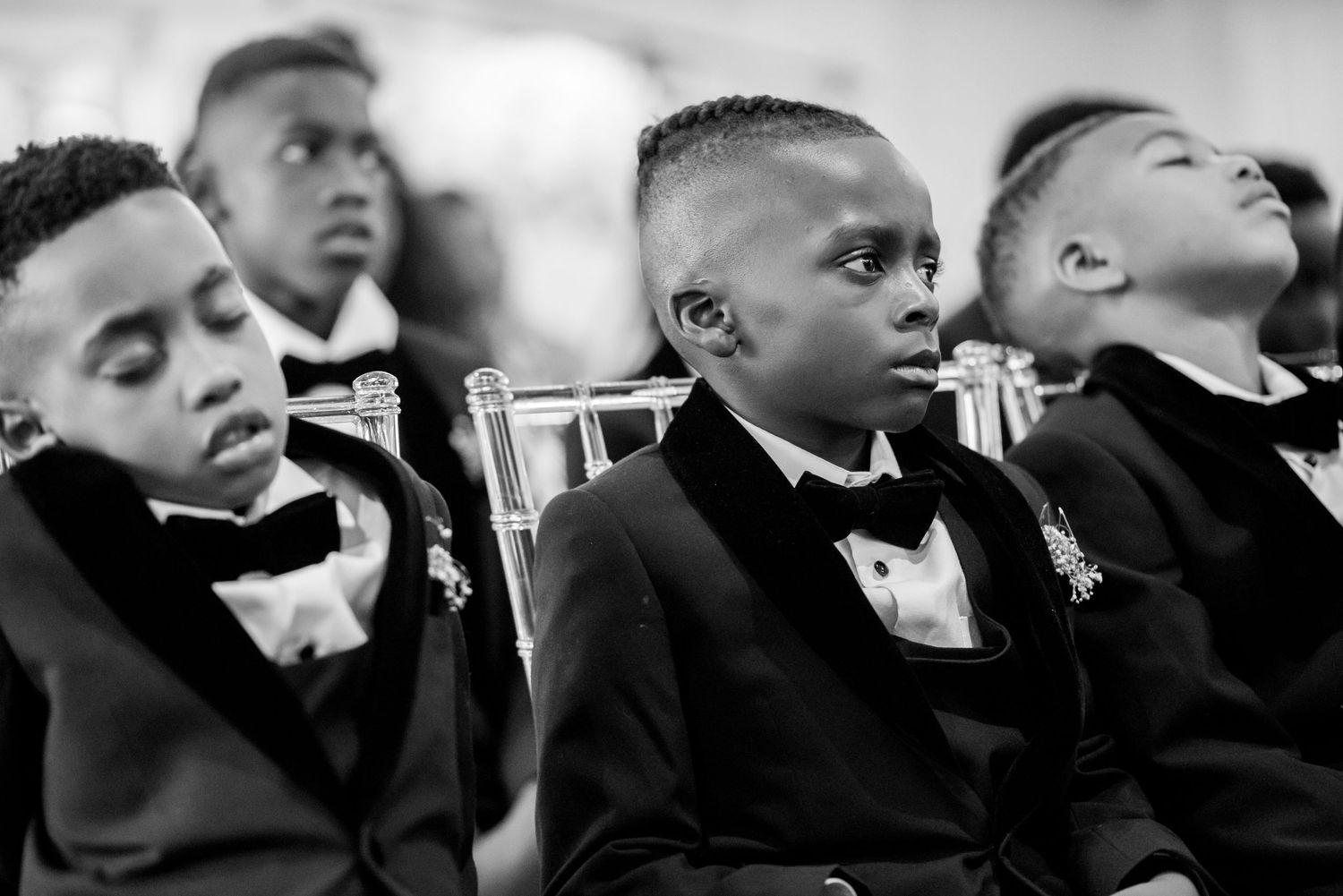 Groomsmen in black tuxedos watching ceremony with serious expressions.