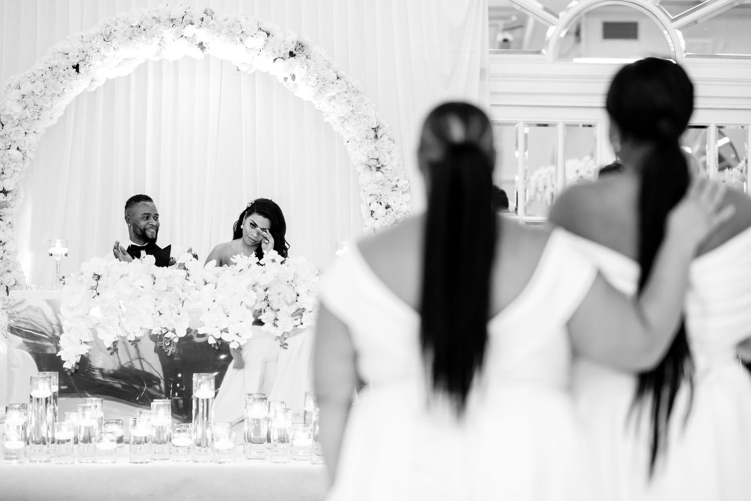 Wedding ceremony space with white floral arch and elegant seating arrangements in monochrome.