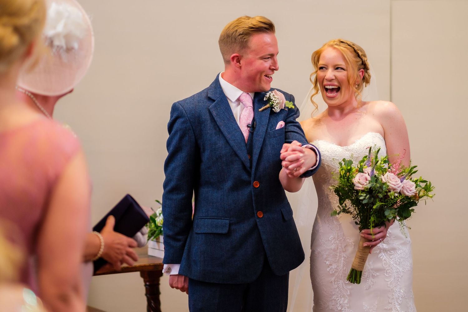Joyful couple laughing and dancing together at their wedding ceremony in formal attire with flowers.