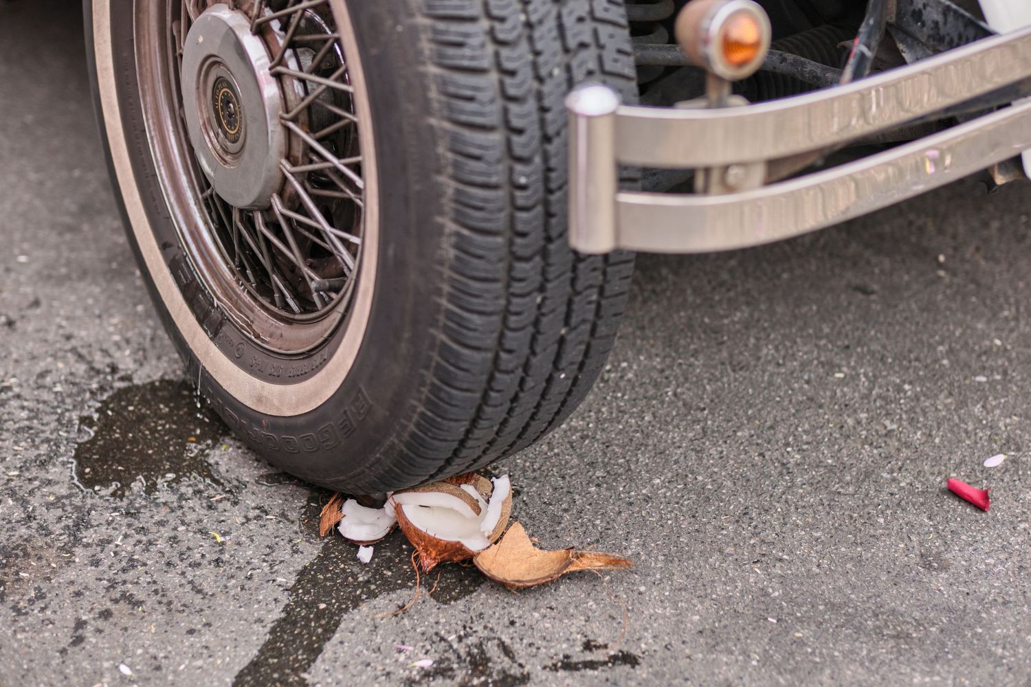 Wedding shoe under vintage car wheel on wet pavement.