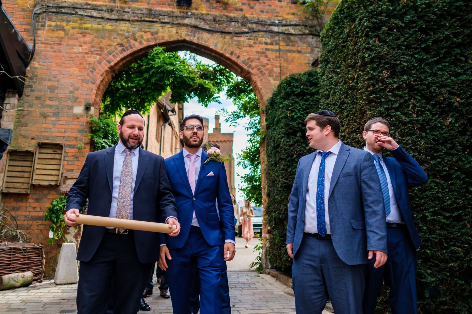Wedding guests mingling under brick archways in garden setting.