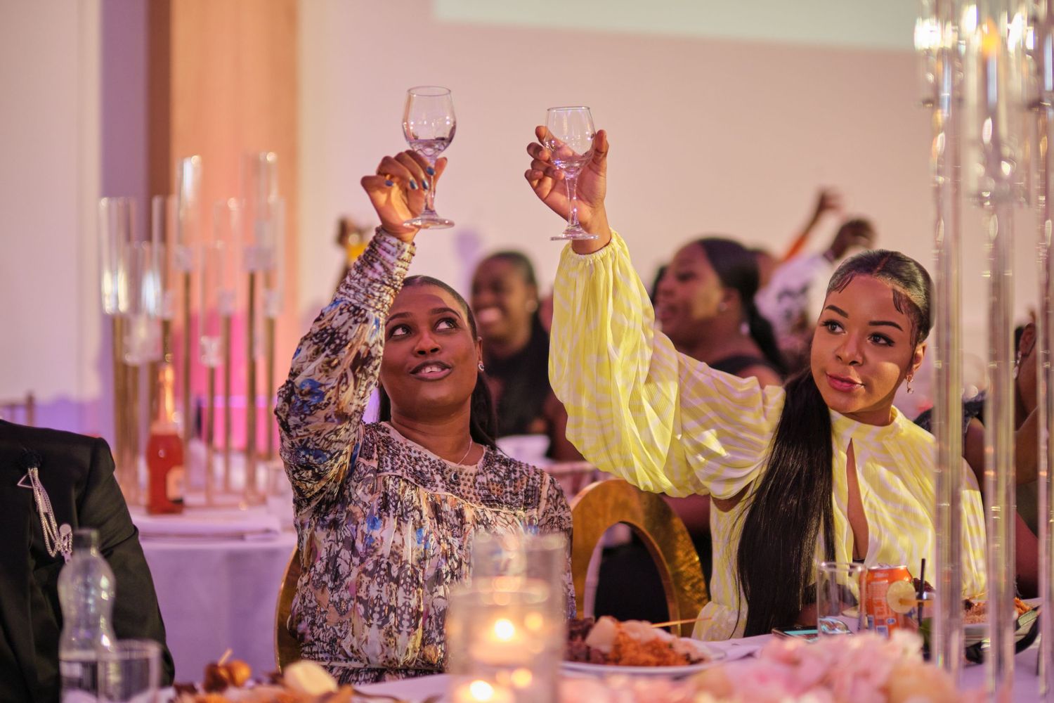 Wedding reception guests celebrating and raising hands during a festive moment under ambient lighting.